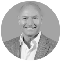 Smiling bald man in a white shirt and tweed jacket, in a black and white circular portrait, looking confidently at the viewe…