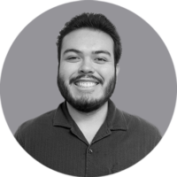 Smiling Man Headshot, Our Team Member Smiling young man with dark hair and beard, wearing a collared shirt, in a black and white circular headshot.